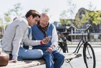 Старший мужчина и взрослый внук на скамейке — стоковое фото