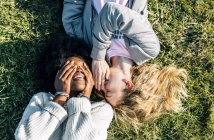 Amici raccontando segreti che giacciono in erba — Foto stock