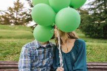 Couple kissing behind green balloons — Stock Photo