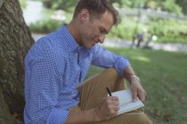 Mann mit Notizbuch sitzt im Park — Stockfoto