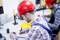 Hombre en fábrica usando sombrero duro tomando notas - foto de stock