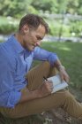Mann mit Notizbuch sitzt im Park — Stockfoto