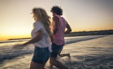 Friends holding hands and running into sea at dusk — Stock Photo