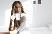 Femme assise sur le lit avec une tasse de café — Photo de stock