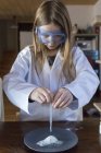 Girl wearing work coat and safety glasses using chemistry set at home — Stock Photo