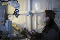 Hombre mirando el brazo robot en una planta de tecnología de sensores - foto de stock