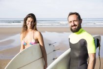 Couple de surfeurs avec des planches de surf au bord de la mer regardant la caméra — Photo de stock