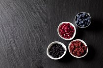 Vista dall'alto di mirtilli con semi di melograno, lupi e chokeberries in ciotole — Foto stock