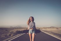 Усміхаючись молода жінка з longboard стояти під порожній сільська дорога — стокове фото