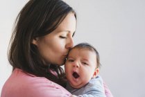 Femme tenant et embrassant un bébé bâillant — Photo de stock