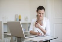 Mãe freelancer com bebê em sling trabalhando no escritório em casa — Fotografia de Stock