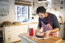 Man standing in kitchen and garnishing ring cake — Stock Photo