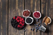 Different berries and seeds in bowls on wooden background — Stock Photo