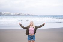 Блондинка молода жінка, стоячи на пляжі з закритими очима і зброї розкритими — стокове фото