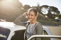 Ritratto di giovane donna sorridente appoggiata sul tetto dell'auto — Foto stock