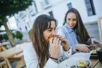Два усміхнених жінок їдять гамбургери в ресторані тротуар в Іспанії, в Андалусії, Vejer-де-ла-Фронтера — стокове фото