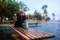 Spagna, Catalogna, Barcellona, Giovane donna che ascolta musica con smartpone seduta su una panchina — Foto stock