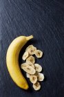 Ansicht von ganzen und in Scheiben geschnittenen Bananen auf schwarzer Schieferoberfläche — Stockfoto