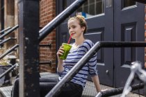 Retrato de jovem mulher sentada em escadas com smoothie verde — Fotografia de Stock