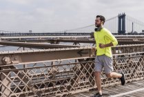 USA, New York, New Jersey, Manhattan view, Young man with headphones jogging at bridge — Stock Photo