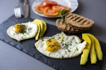 Closeup view of fried eggs with toasts and avocado — Stock Photo