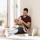 Батько зціджування дитину сина, сидячи на килимі — стокове фото