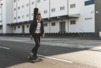 Jeune homme avec caisse de guitare équitation skateboard dans la rue — Photo de stock