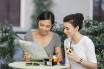 Дві молоді жінки разом дивлячись на карту на тротуарі кафе — стокове фото