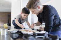 Padre e hijo preparando pizza en la cocina juntos - foto de stock