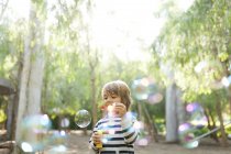 Porträt eines Jungen, der Seifenblasen im Freien pustet — Stockfoto