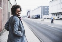 Souriant jeune femme sur le trottoir regardant caméra — Photo de stock