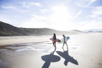 Coppia di surfisti con tavole da surf sulla spiaggia sabbiosa alla luce del sole — Foto stock