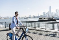 Hombre en bicicleta en el paseo marítimo de Nueva Jersey con vistas a Manhattan, EE.UU. - foto de stock