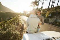 Young couple in love sitting on car bonnet at roadside in nature — Stock Photo
