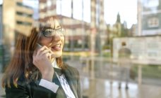 Businesswoman talking on phone in front of glass pane — Stock Photo