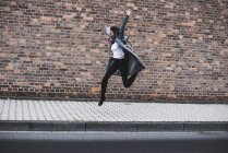 Молода жінка з навушниками і рюкзак, стрибки в повітря перед цегляна стіна — стокове фото