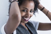 Porträt einer lächelnden jungen Frau mit den Händen im Haar, die in die Kamera blickt — Stockfoto