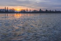 Alemanha, dois patinadores no gelo congelado Lago Constance com Reichenau Island no fundo ao pôr-do-sol — Fotografia de Stock