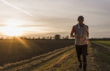 Retrato de jovem correndo em campo ao pôr do sol — Fotografia de Stock