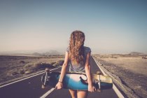 Blond young woman with longboard standing on empty country road — Stock Photo