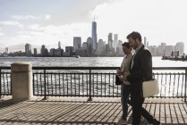 États-Unis, New York, Brooklyn bridge, Jeune homme casqué à vélo avec smartphone, paysage urbain en arrière-plan — Photo de stock