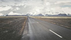 Islanda, strada di campagna vuota con montagne innevate sullo sfondo — Foto stock
