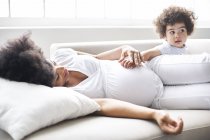 Pregnant woman and little son lying on sofa at home — Stock Photo