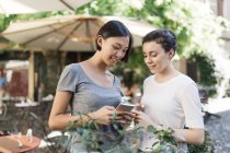 Dos mujeres jóvenes compartiendo teléfono inteligente en el café de la acera - foto de stock