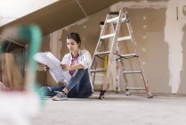 Portrait of young woman sitting on floor with construction plan — Stock Photo