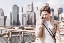 USA, New York, Brooklyn bridge, Femme mûre au téléphone, Paysage urbain en arrière-plan — Photo de stock