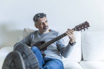 Portrait of mature man playing guitar on sofa — Stock Photo