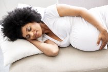 Mulher grávida relaxante com os olhos fechados no sofá — Fotografia de Stock