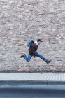 Young man jumping in front of brick wall — Stock Photo