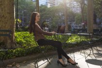 Jeune femme d'affaires travaillant au parc de la ville assis avec ordinateur portable à la table au soleil — Photo de stock